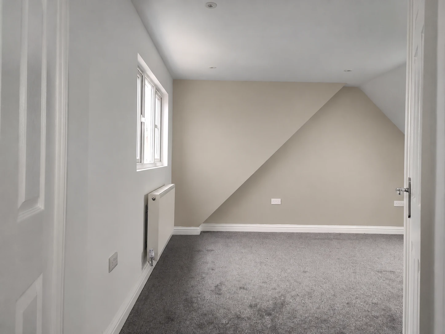 Corby loft bedroom with a dormer window and grey carpet; feature wall digitally recoloured to warm stone