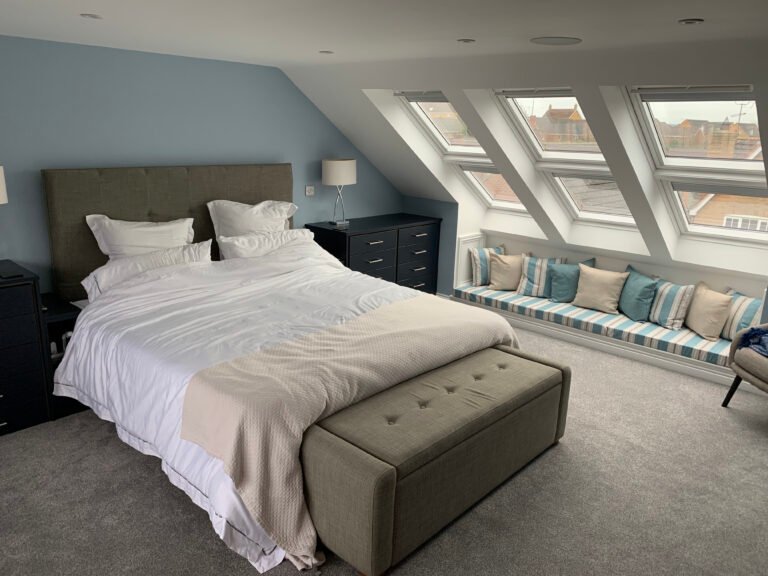 Finished Crane Close loft bedroom with three rooflights, a cushioned window seat, pale blue walls and grey carpet