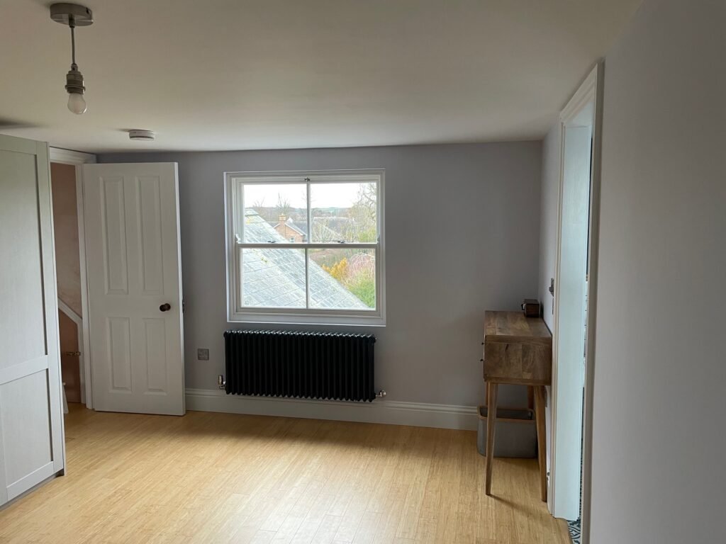 Loft bedroom at Station Road, Oakham, with a sash window, dark radiator and timber-effect flooring